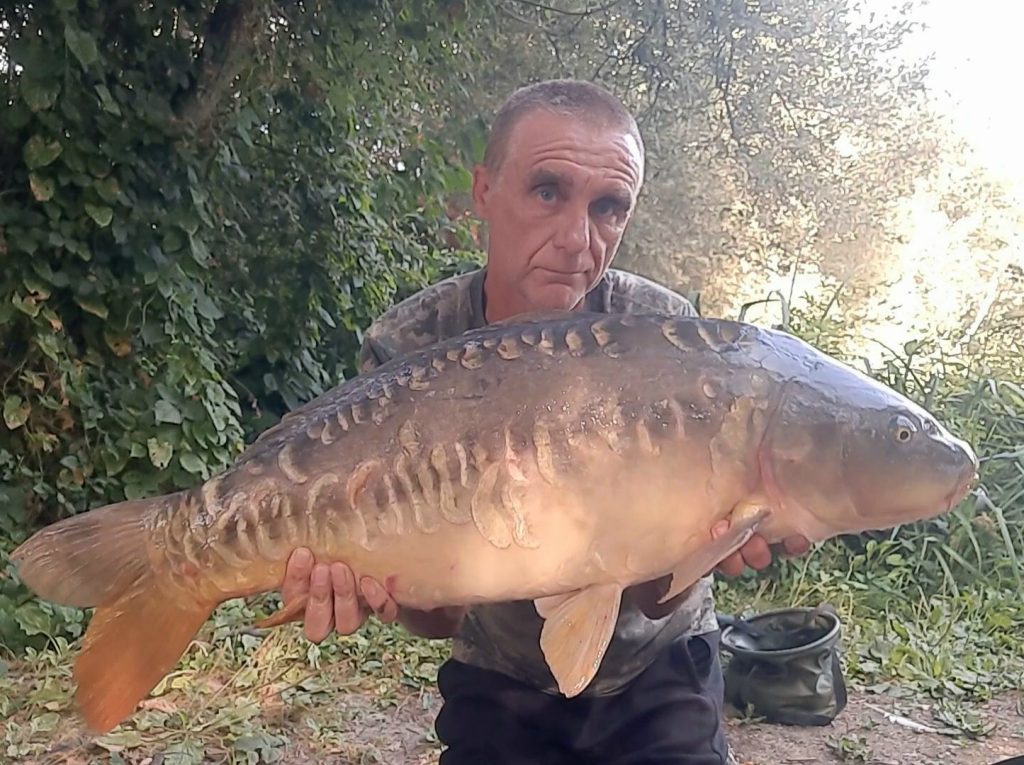 Angler holding a large heavily scaled mirror carp caught from Whelford Pools Top Lake, Fairford, Gloucestershire
