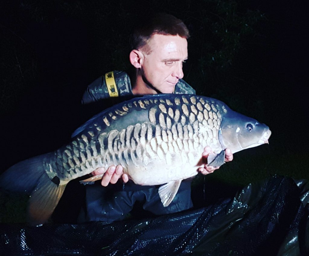 Angler holding a large heavily scaled mirror carp caught during a night session at Shearwater Lake, Warminster, Wiltshire
