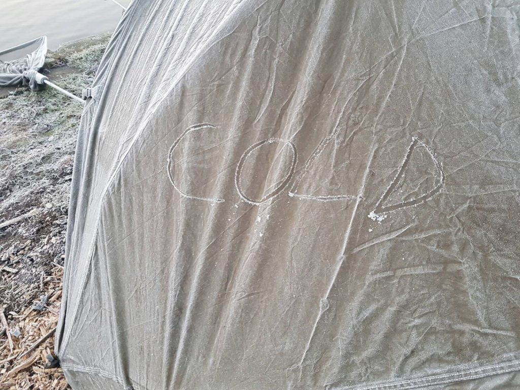 Frost-covered bivvy tent with the word "COLD" drawn into the icy canvas on a freezing winter carp fishing session.